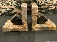 Pair of two L-shaped marble bookends with black pyramid accent pieces placed on a black surface, showing side profile and top surfaces.