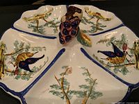 Close-up of the sectioned dish showing the detailed hand-painted birds, leaves, and branches design with grapes cluster handle