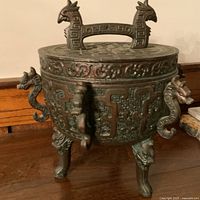 Front angle showing dragon head handles, leg details, embossed motifs and bird-shaped lid handle