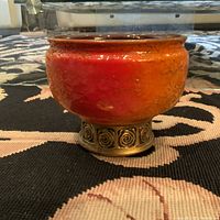 Front side view of the ceramic bowl/candle holder showing red-orange textured glaze and metallic spiral base.