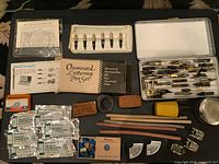 Overview of entire vintage pen and writing utensil collection laid out showing tin case filled with pens, nib sets, drawing guides, pencils, sharpeners, and ink.