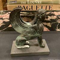 Front view of the vintage sphinx statue showing detailed wings, human head with braided hair, and lion body mounted on a rectangular slate base.