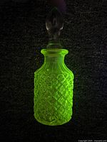 Perfume bottle glowing bright green under blacklight showing diamond hatch pattern and clear stopper.