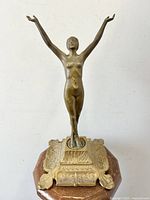 Front view of full statue showing raised arms and octagonal decorative base