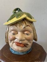 Front-facing close-up of the humorous drunk character humidor head showing facial details and leafy lid with cigar in mouth.