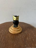 Front view of the bronze owl figurine on stepped wooden base showing gold-colored face and black body.