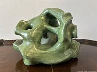 Left front angle view of green biomorphic pottery sculpture showing organic form with openings and smooth glaze.
