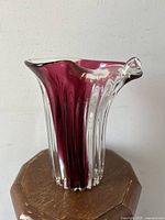 Clear and deep red striped Murano glass vase with scroll edge from a front angle on a wooden surface.