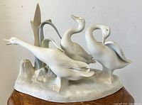 Front view of the Lladro porcelain duck trio sculpture placed on a wooden table showing all three ducks and detailed base.
