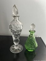 Clear and green etched antique perfume bottles with stoppers shown together front angle