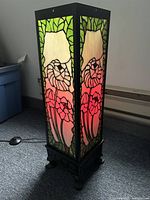 Front three-quarter view of lamp lit, showing floral stained glass panels, metal frame, and foot switch visible.