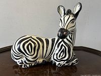 Side view of ceramic zebra figurine showing detailed black and white striped pattern and pink nose.