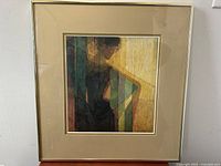 Framed modernist lithograph showing abstract figure with geometric color blocks in earthy tones, beige frame with gold accents.