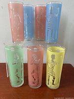 Photo of seven tall cylindrical highball glasses in pastel colors with illustrations of striped bathing suit figures "The Bathers" by Dominion Glass.