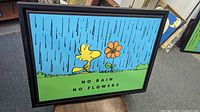 Framed Peanuts print front view showing Woodstock, flower, and rain design with text 'NO RAIN NO FLOWERS'.