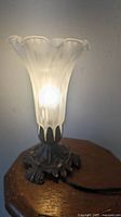 Front view of the vintage lily-shaped table lamp illuminated, showing frosted white glass shade and decorative base.