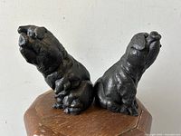 Two seated pig cast-iron bookends shown side by side on wooden surface, displaying front and side views