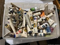 Plastic container filled with around 40 tubes of Jo Sonja's acrylic paint tubes, mostly 75 ml. Various colors visible, tubes stacked and lying in random order.