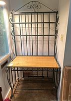 Front view of the metal and wood bakers rack showing the wooden countertop and upper metal bars with scroll details.