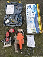 Mastercraft impact driver in hard plastic case with socket adapters, blue power cord, and instruction manual, along with red router and Black & Decker chainsaw outside the case on ground.