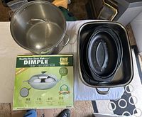 Set of cookware including stockpot, two roasting pans, and boxed non-stick wok arranged on white cloth