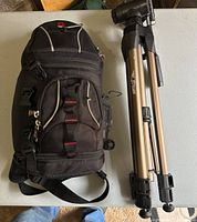 Black padded camera bag and aluminum tripod side by side on a table