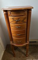 Front view of the tall wooden jewelry cabinet showing five drawers with decorative handles and fluted columns on sides.