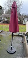 Full view of closed burgundy patio umbrella with black pole and base in outdoor setting.
