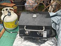 BBQ grill with propane tank connected by hose, showing full setup on table