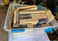 Top-down view of multiple cradled wood panels inside a plastic tote, showing various sizes and shapes including rectangular and oval.