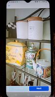 Photo showing shelf with white textured canisters with wooden lids, yellow biscotti jar, Asian ginger jar, and floral teapot.