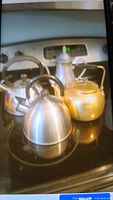 Four metal kettles displayed on stove top showing variety of finishes including stainless steel and brass