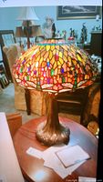 Full view of Tiffany style lamp with colorful stained glass dome and detailed ornate metal base on wooden surface.