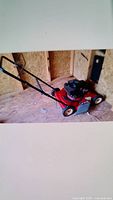 Side view of red Craftsman gas lawn mower inside a shed with black handle and engine cover, showing wear and dust.
