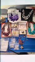 Full lot of assorted necklaces and earrings displayed on blue cloth including boxed sets and bagged earrings.