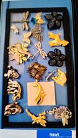 Display of 19 assorted pins on blue backing, including animals, dragonflies, floral motifs, and fairies in gold, silver and black finishes.