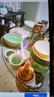 Photo showing several pottery pieces including a green glazed bowl, white mortar and pestle, a ceramic owl with pedestal, orange and green glass bowls, and a ceramic jug with olive oil on a glass table.