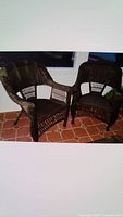 Two brown rattan outdoor chairs placed indoors on a reddish-brown tile floor near a window.