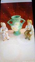 Lot showing green Roseville vase with floral design flanked by two Japanese figurines of an elderly man and woman sitting.