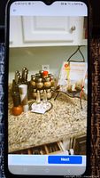 Overall view of spice rack with nine glass spice jars with brass lids, salt and pepper grinders, plus two cookbooks displayed on a black wire stand on granite countertop.