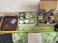 Full view of tea set including teapot, bowls in packaging, and decorative tray with measuring tape for scale.
