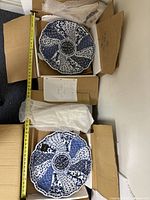 Two large blue and white decorative plates in original boxes, each approximately 12 inches in diameter, with measuring tape shown for scale.