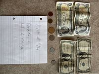 Photo showing Canadian and US paper bills and coins on a carpeted floor with a handwritten note indicating Lot #44 containing Canadian and US currency.