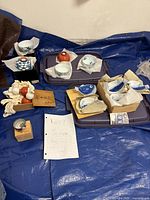 Overview of ceramic dishware set spread out on a blue tarp, showing multiple small bowls, original boxes, and fish-shaped plates wrapped in protective paper.