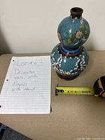 Front view of the cloisonné vase standing on a wooden display stand with measuring tape beside it showing height.