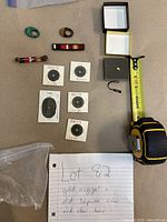 Overview: two plastic rings, two enamel ribbon bars, brass ingot bar, six Japanese cast coins mounted in holders, gold nugget in box, small metal hook