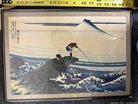 Front of framed artwork showing Japanese fisherman print with Mount Fuji in background and measuring tape above.