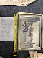 Photo showing framed artwork laid flat with a tape measure indicating width around 14 inches alongside paper note indicating title and description.