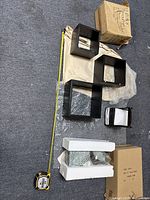 Photo of black square wall shelves of different sizes laid out on floor with protective wrapping and cardboard boxes nearby.