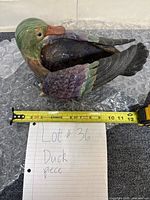 Top side view of multicolor ceramic duck figure on bubble wrap with tape measure showing close to 10.5 inches long.